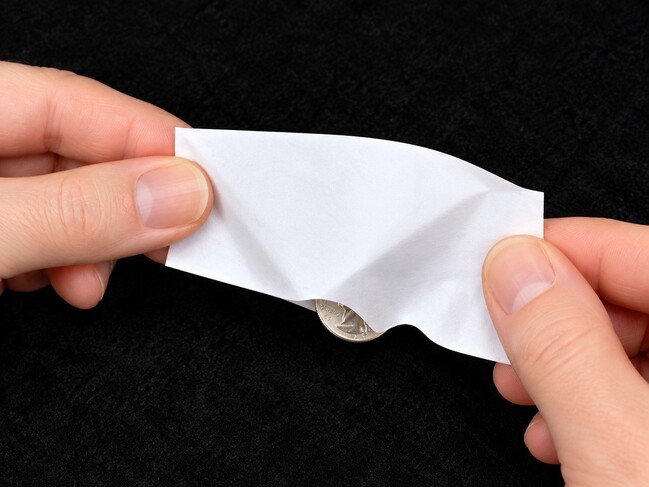 Big coin squeezing through small hole in paper sheet.