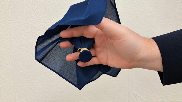 Elastic band being slipped around the coin through the handkerchief