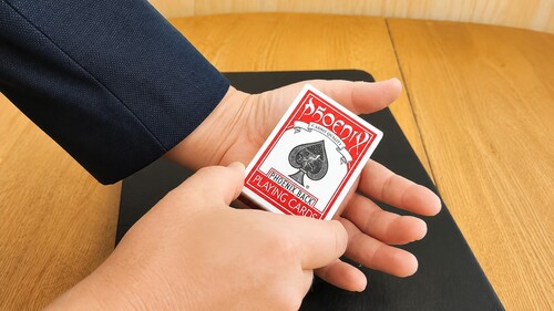 Boxed deck of playing cards placed into the hand concealing the duplicate coin