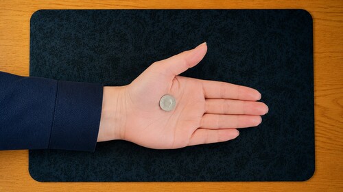 A coin resting near the base of the thumb in an open palm