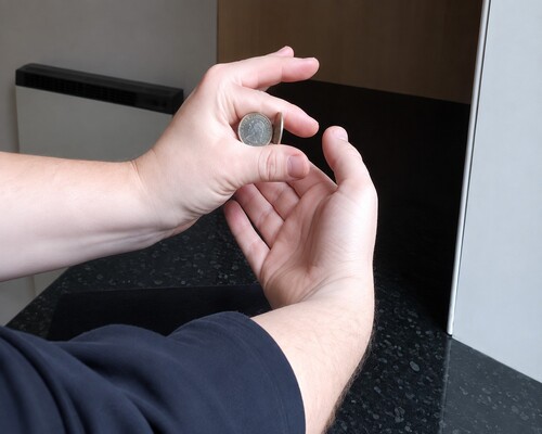 The other hand approaching from below to cover and take the displayed coin