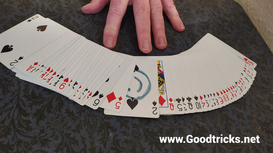 Deck of cards are fanned out on table, face up.