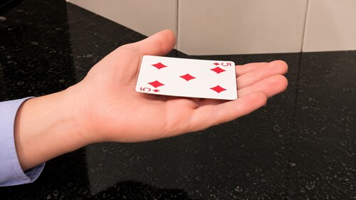 A gimmicked playing card resting flat on the magician's open palm