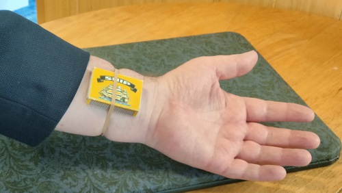 A full matchbox secured behind the left wrist with a rubber band