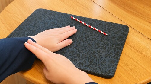 Magician waving a hand beside a straw on a wooden table
