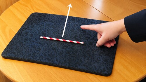 Finger moving away as a straw follows across a wooden table