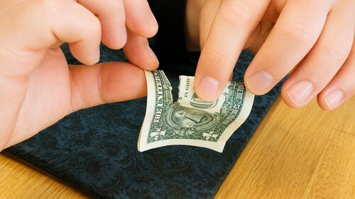 A short tear being made in a folded dollar bill