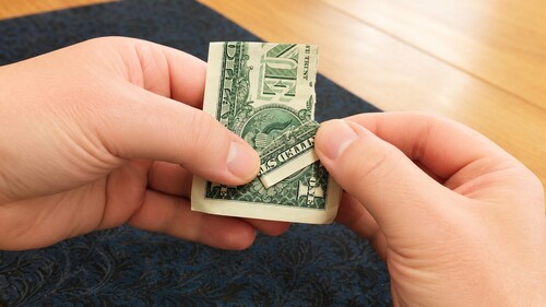 Torn flap of a dollar bill being folded flat and held with the thumb