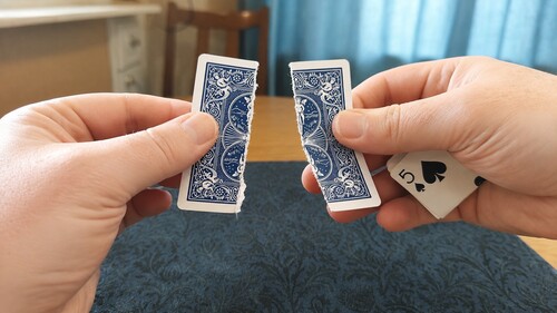 A playing card being torn lengthwise along its crease